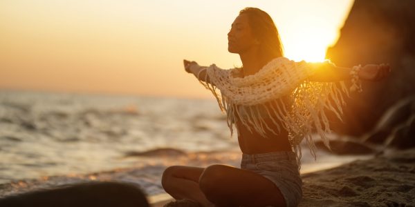 Carefree woman with arms outstretched enjoying in freedom while relaxing on sand at the beach during sunset.